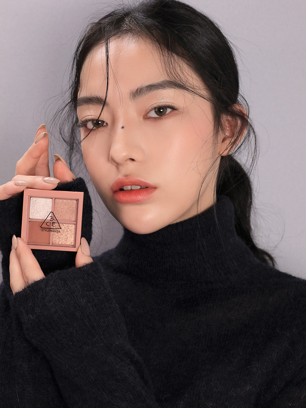 Model in black turtleneck holding 3CE Mini Multi Eye Color Palette in Shade Second Pair, showcasing wearable versatility.