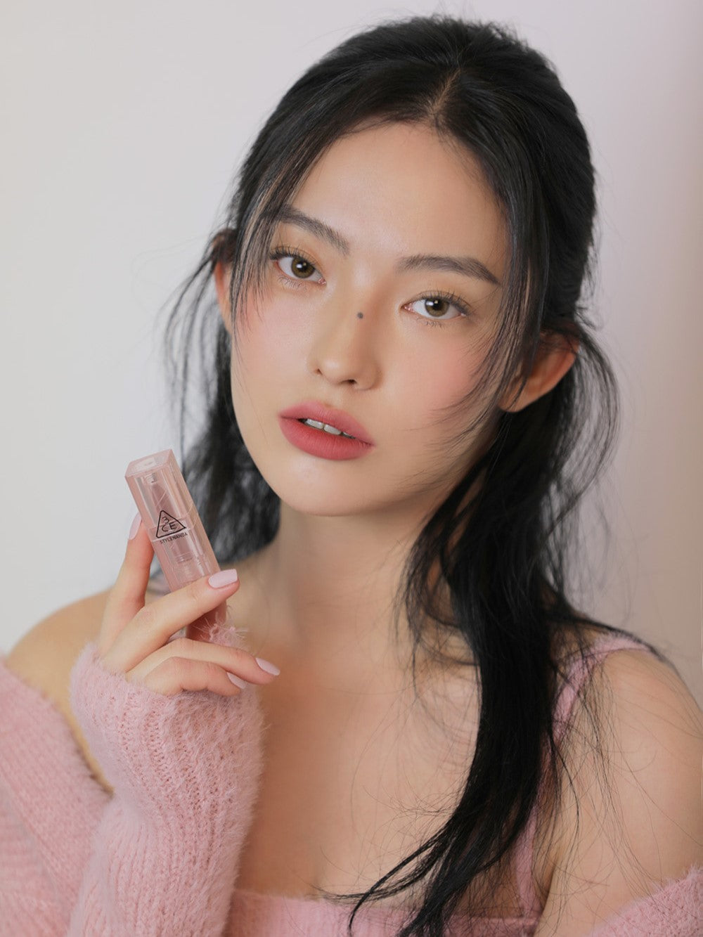 Model holding 3CE Soft Matte Lipstick in Shade Hazy Rose, emphasizing its velvety texture and comfortable matte wear.