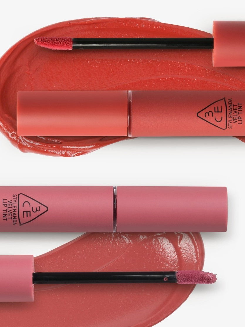 Two 3CE Velvet Lip Tint tubes with applicators placed over vibrant coral and pink swatches, showcasing smooth texture and rich pigmentation.