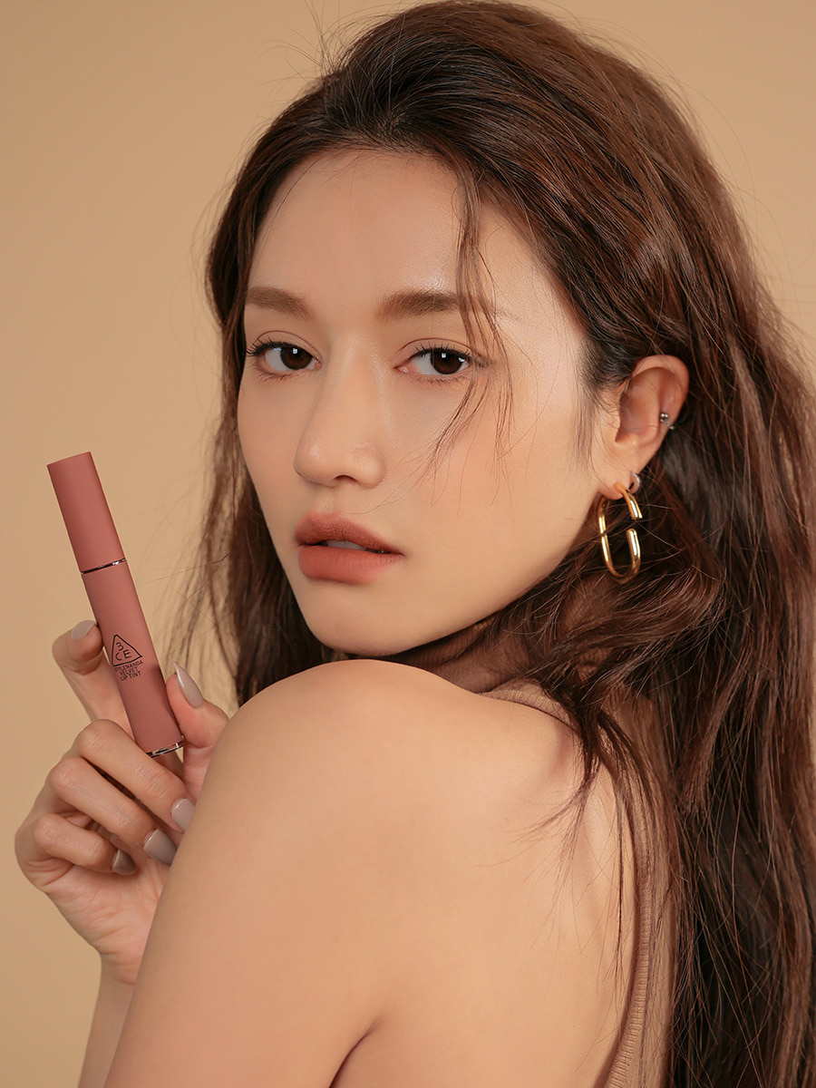 Model wearing gold hoop earrings against a muted beige background displaying 3CE Velvet Lip Tint in Shade Walk N Talk, highlighting the product’s creamy texture and bold pigmentation.