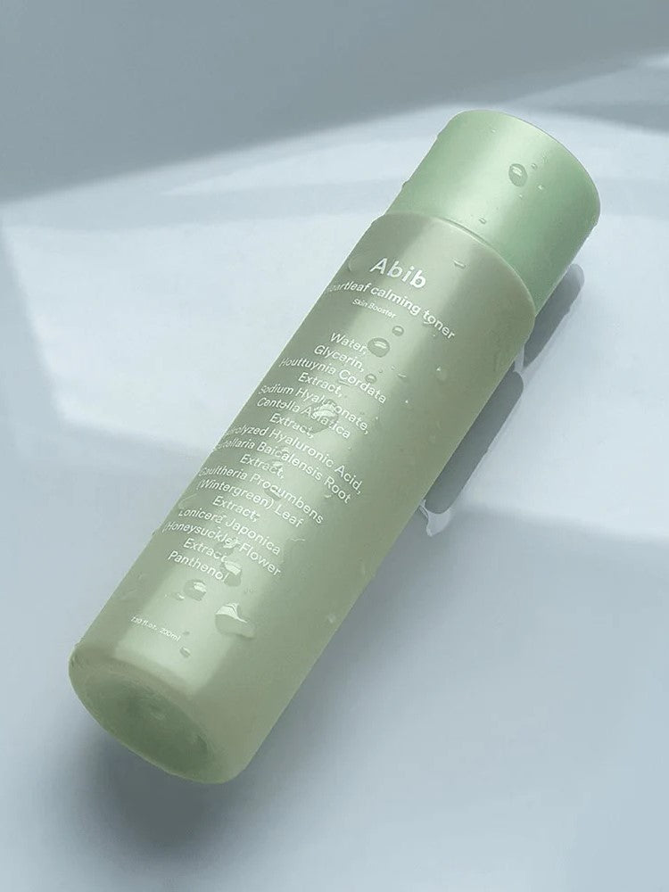 A green bottle of Abib Heartleaf Calming Toner with water droplets, showcasing its calming and hydrating properties.