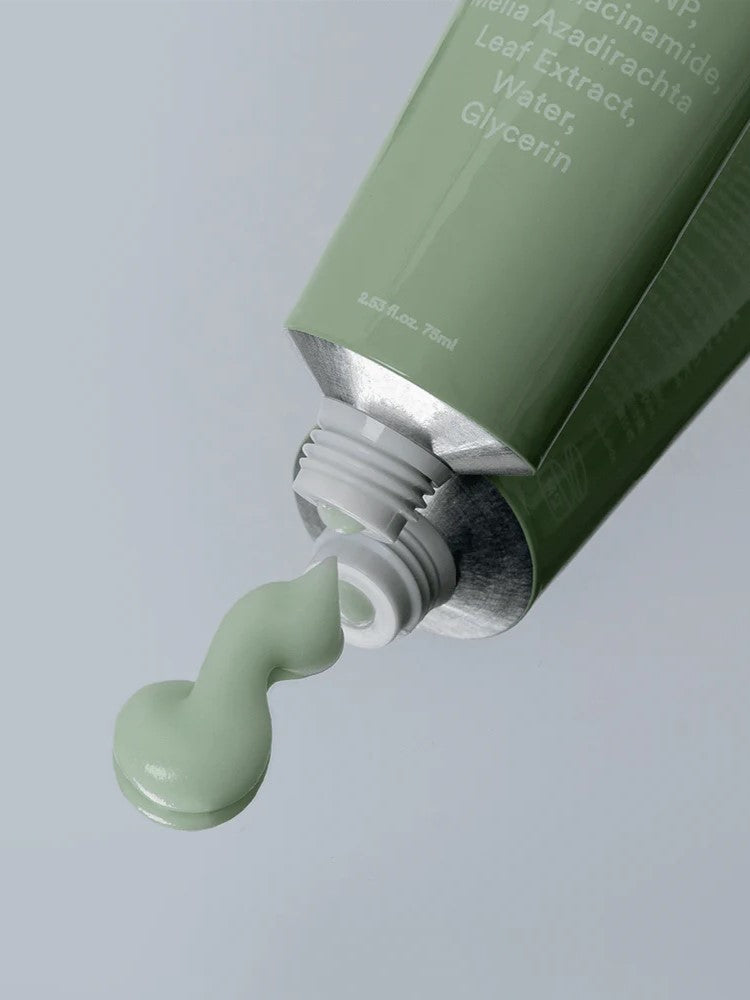 The Heartleaf Crème Calming Tube by a0d026 dispenses light green cream enriched with hyaluronic acid from its green tube. White text, partially visible on the tube, lists ingredients as the cap is removed. The background features a subtle, neutral light gray shade.