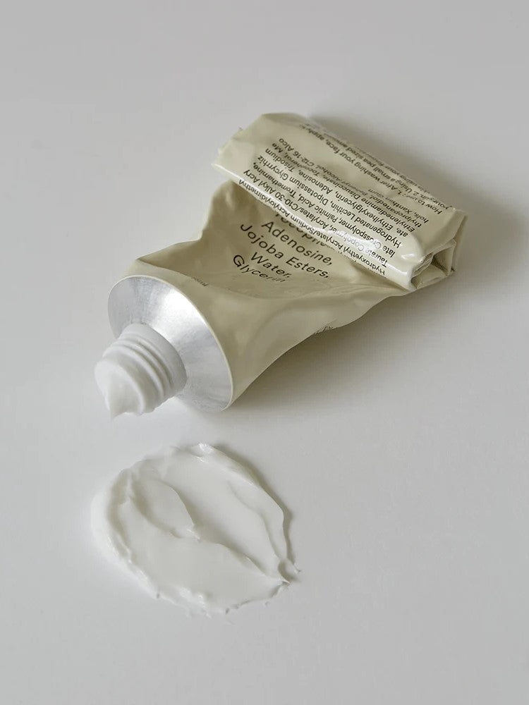 A squeezed tube of the Abib Jericho Rose Crème with a silver cap, placed beside a dollop of white cream on a light surface, showing the product texture.