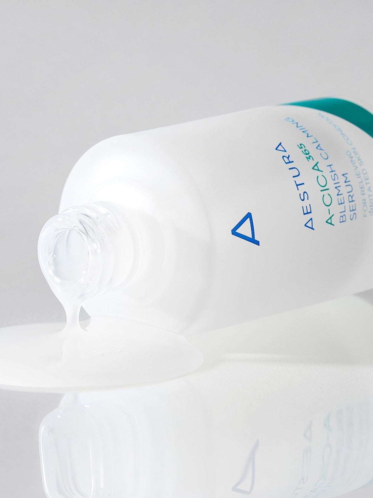 A partially spilled bottle of Aestura A-Cica 365 Blemish Calming Serum with its clear, smooth serum pooling on a reflective surface.