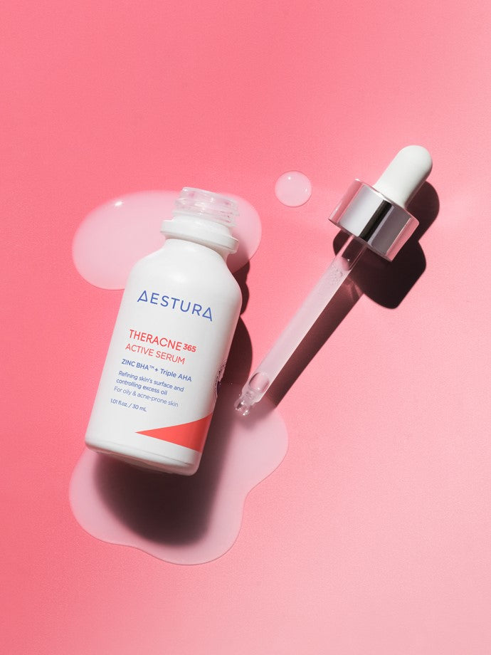 A bottle of Aestura Theracne 365 Active Serum with a dropper, resting on a soft pink surface, with serum pooling beneath.