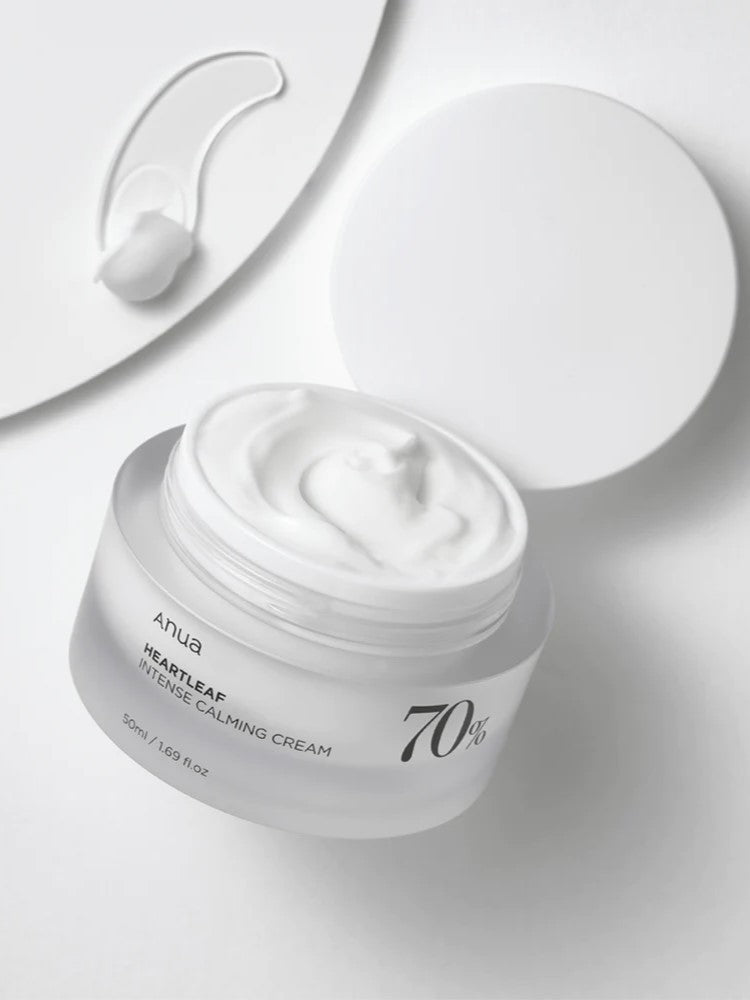 A jar of Anua Heartleaf Intense Calming Cream with a smooth, thick texture, accompanied by a spatula and lid on a white background.