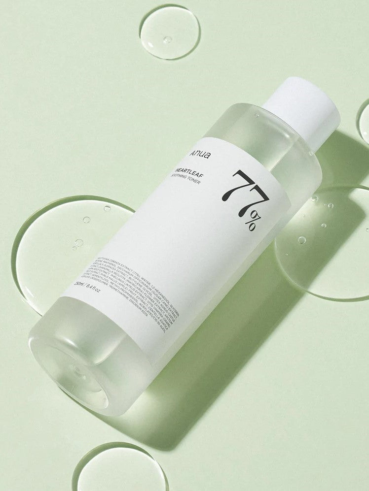 A clear bottle of Anua Heartleaf 77% Soothing Toner on a soft green background, with droplets of its lightweight texture visible on the surface.