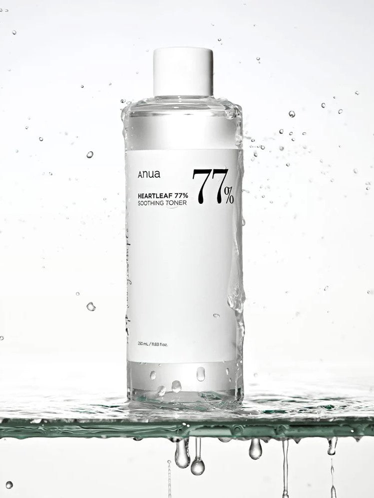 A clear bottle of Anua Heartleaf 77% Soothing Toner, splashed with water droplets, set against a minimalist white background.