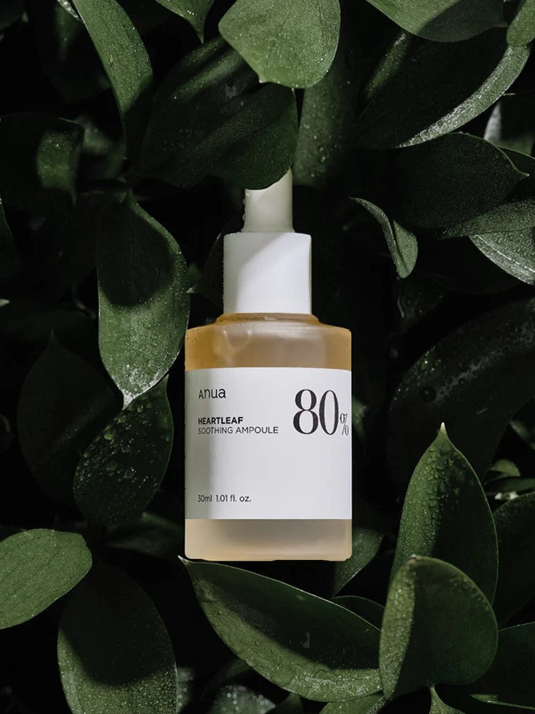A bottle of Anua Heartleaf Soothing Ampoule surrounded by green heartleaf leaves, showcasing its natural skincare appeal.