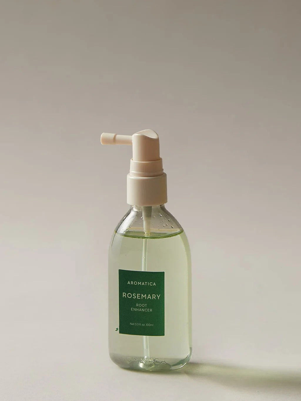 Clear pump bottle of Aromatica Rosemary Root Enhancer hair treatment, shown on a neutral background.