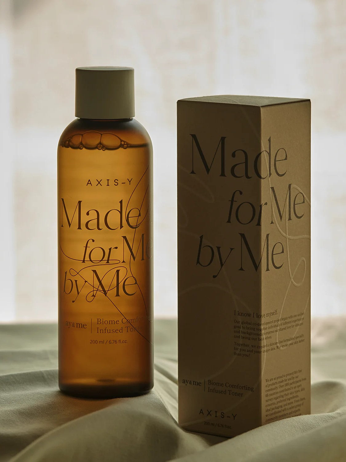 AXIS-Y Biome Comforting Infused Toner standing with its box on a soft fabric background.