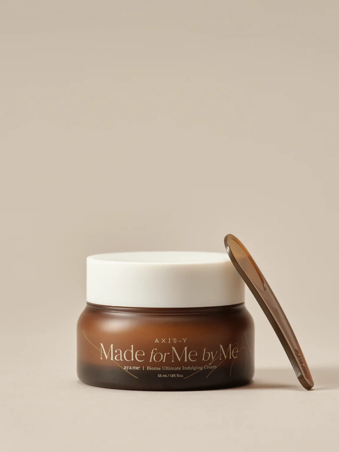 Brown jar of AXIS-Y 'Made for Me by Me' Biome Ultimate Indulging Cream with white lid and brown spatula, set against a beige background.
