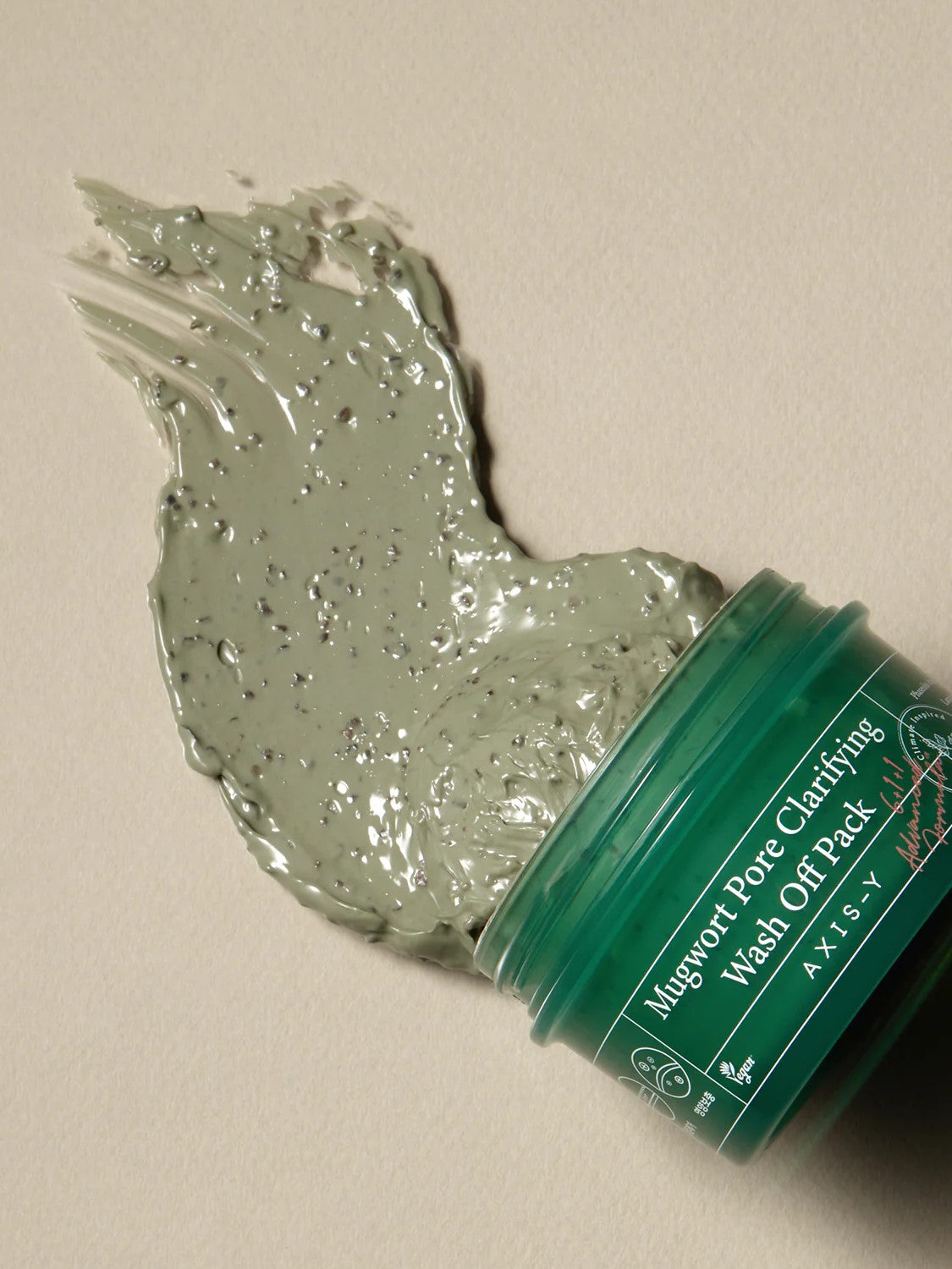 Jar of Mugwort Pore Clarifying Wash Off Pack with green mud-like product smeared beside it, showing texture and exfoliating beads.