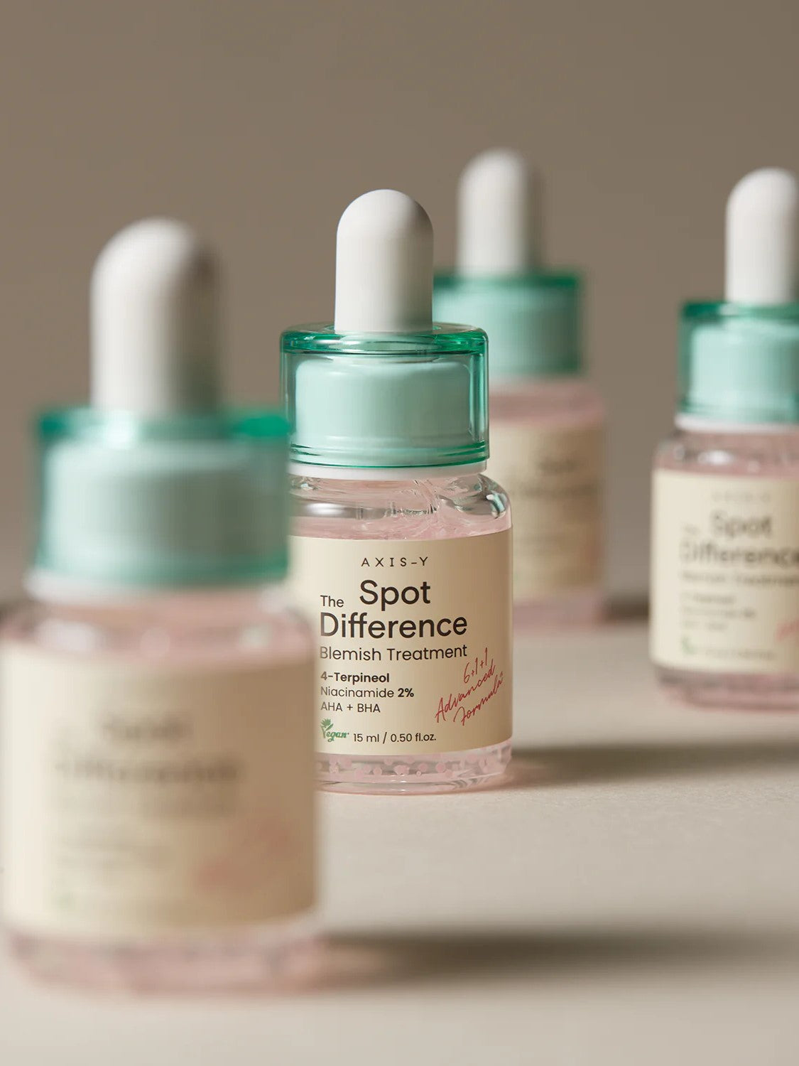 Four bottles of Axis-Y Spot Difference Blemish Treatment with mint green caps and labels, featuring key ingredients like Terpineol, Niacinamide, and exfoliants for blemish care.