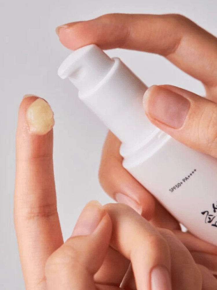 A close-up of a hand dispensing Beauty of Joseon Ginseng Moist Sun Serum onto a fingertip, showcasing its smooth, creamy texture.