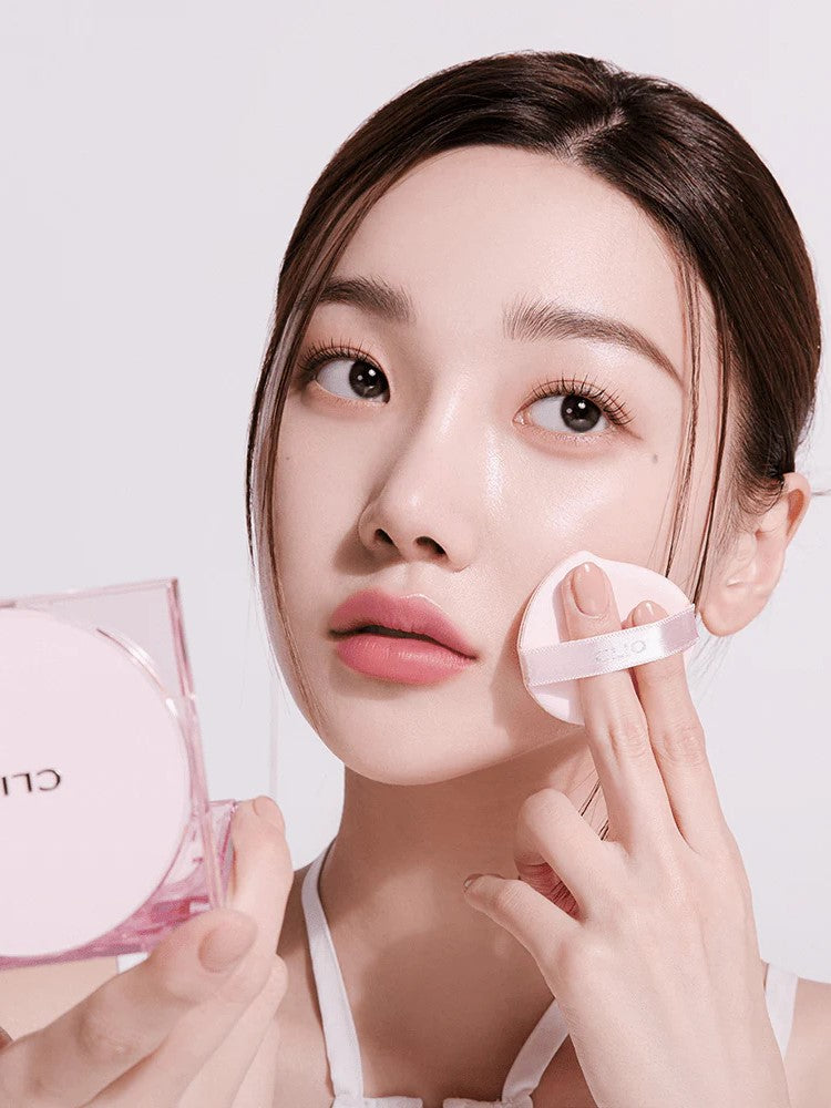 Model with brown hair applying CLIO Kill Cover Mesh Glow Cushion, showcasing radiant glass-skin effect.