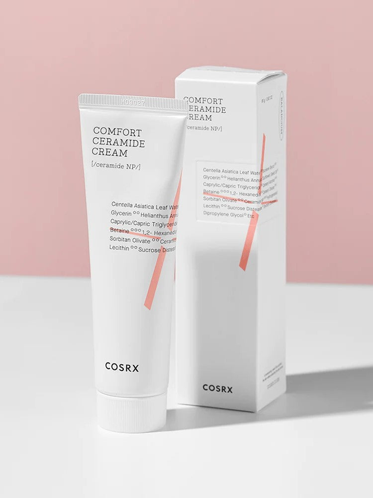 A tube and box of Cosrx Comfort Ceramide Cream against a soft pink background, highlighting minimalist packaging and ingredients list.