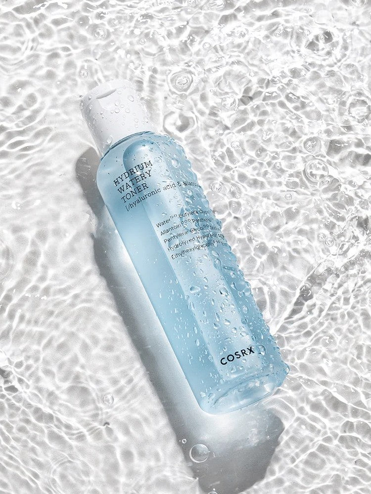 A bottle of Cosrx Hydrium Watery Toner resting on shimmering water, highlighting its refreshing texture with droplets on the surface.