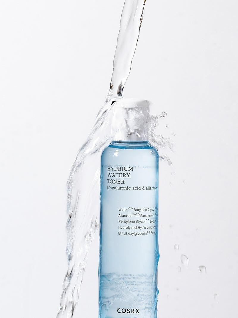 A blue bottle of Cosrx Hydrium Watery Toner splashed with water, emphasizing its hydrating ingredients.