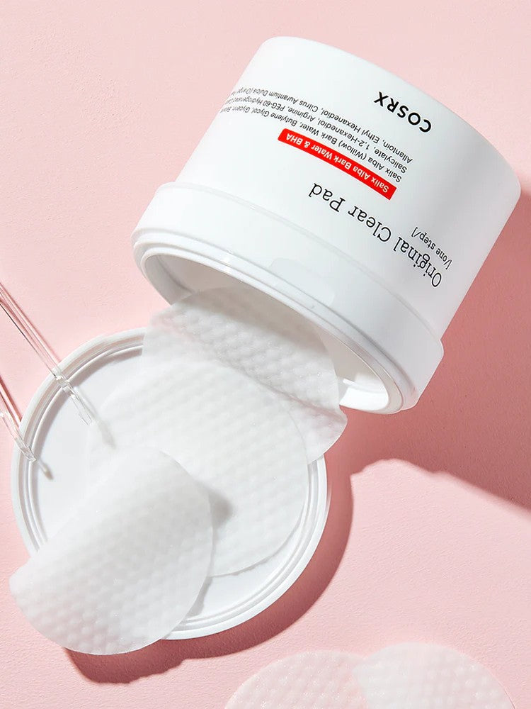 A white jar of COSRX Original Clear Pad with cotton pads partially pulled out, resting on a pink background.