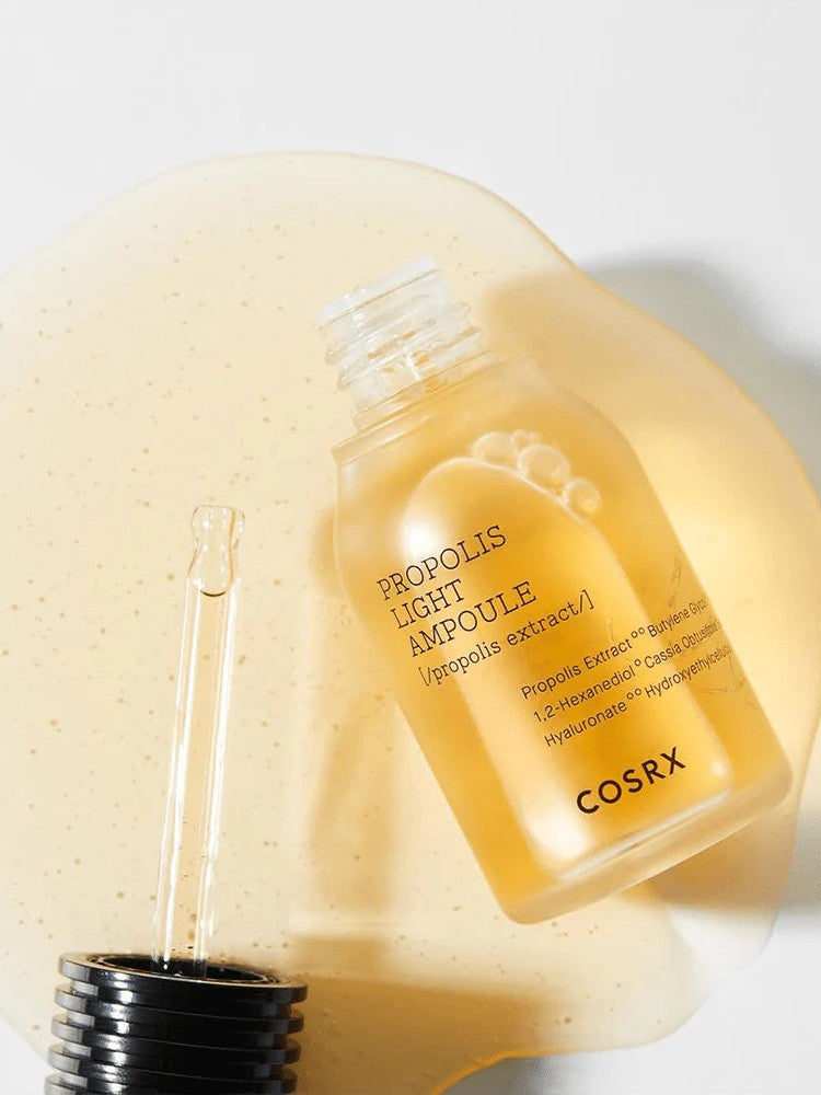 Cosrx Propolis Light Ampoule with dropper, surrounded by its golden, viscous texture resembling honey, highlighting its nourishing and soothing properties.