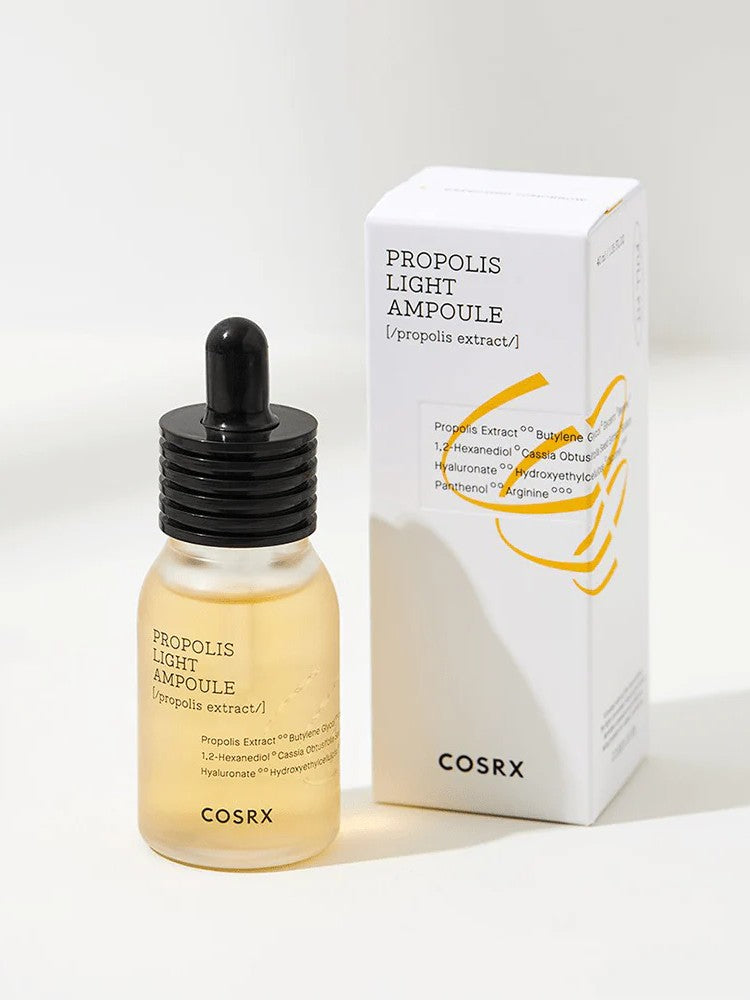 A bottle of Cosrx Propolis Light Ampoule with a dropper, placed beside its minimalist white packaging displaying product details.
