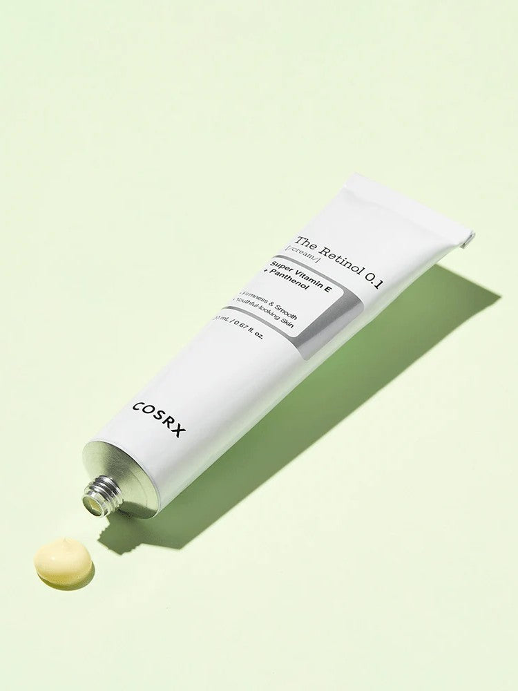 A tube of Cosrx Retinol 0.1 Cream with a small dollop of cream texture next to it, set against a pale green background.