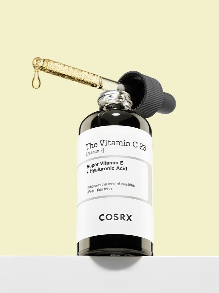 Cosrx The Vitamin C 23 Serum with dropper showcasing its texture, with visible text describing skin health benefits, set against a light yellow background.