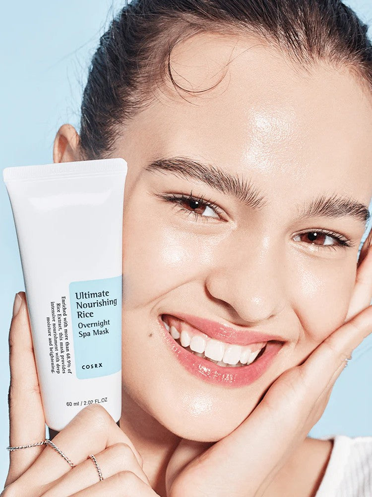 A model holding a Cosrx Ultimate Nourishing Rice Overnight Spa Mask tube, showcasing the mask’s glass skin effect on her glowing complexion.
