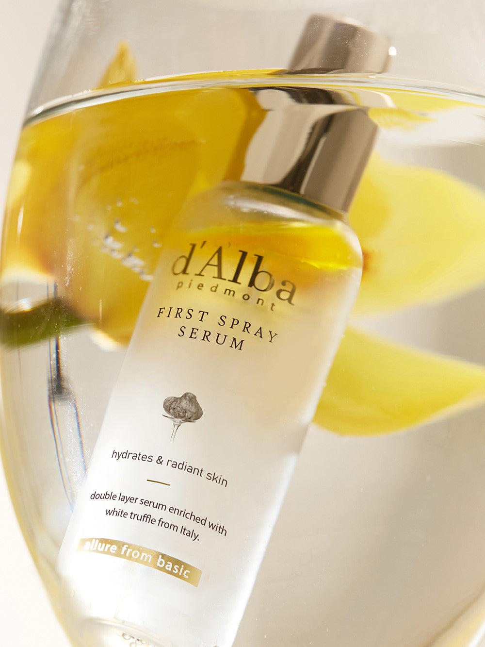 A bottle of d'Alba First Spray Serum with a silver cap, submerged in water, highlighting its dual-layer oil and serum formula.