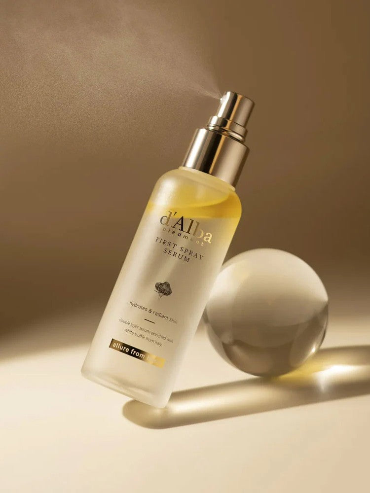 A sleek bottle of d'Alba First Spray Serum with a mist nozzle, set against a soft beige background to evoke luxury and hydration.