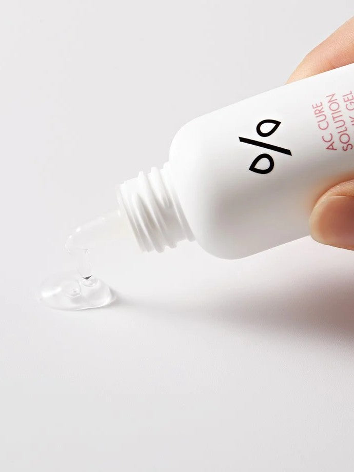 A hand holding a bottle of Dr. Ceuracle AC Cure Solution Pink Gel, with a clear gel droplet spilling onto a plain surface, showcasing its lightweight and soothing texture.