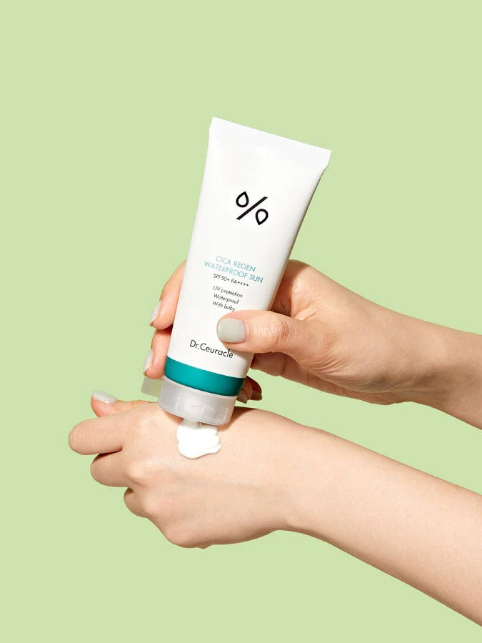 A hand squeezing Dr. Ceuracle CICA Regen Waterproof Sun Cream onto another hand against a light green background, highlighting its creamy yet lightweight texture.