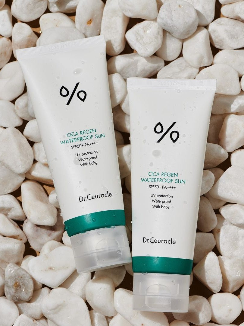 Two tubes of Dr. Ceuracle CICA Regen Waterproof Sun Cream with SPF 50+ PA++++, surrounded by white pebbles and water droplets, highlighting its waterproof formula and suitability for babies as indicated on the labels.