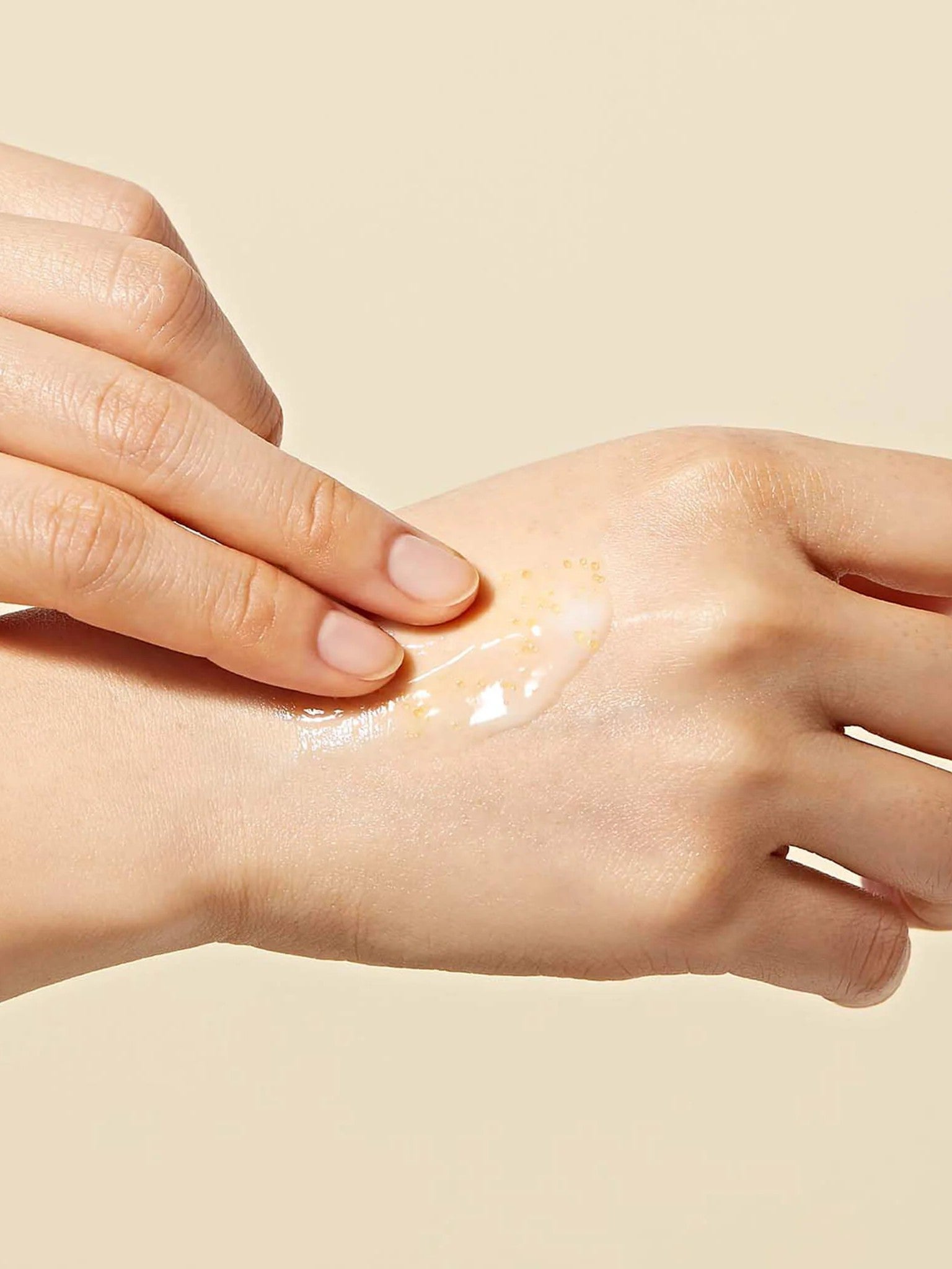 A hand applying Dr. Ceuracle Royal Vita Propolis 33 Capsule Eye Cream, featuring small Propolis beads in the texture, onto skin against a soft beige background.