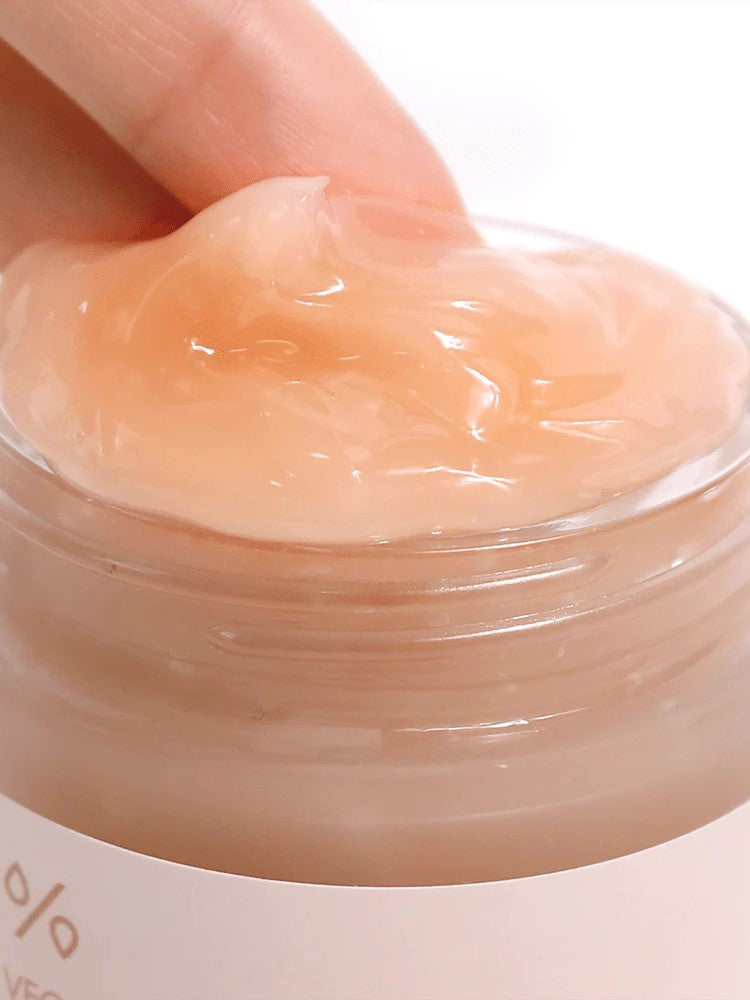 A close-up of a hand dipping into a translucent, peach-colored jar of Dr. Ceuracle Vegan Kombucha Tea Gel Cream, showcasing its smooth, gel-like texture.