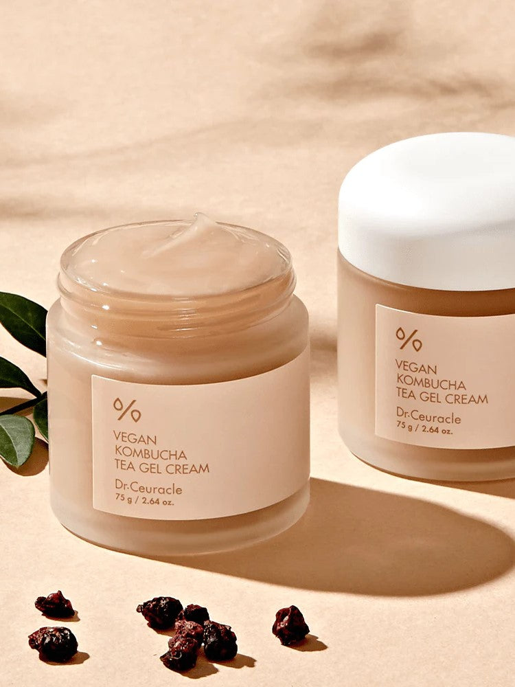 Two jars of Dr. Ceuracle Vegan Kombucha Tea Gel Cream on a beige background, surrounded by dried berries and green leaves, highlighting its antioxidant-rich formula.