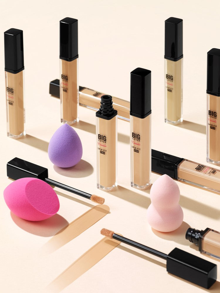 Aesthetic arrangement of Etude House Big Cover Skin Fit Concealer PRO foundation tubes, concealer wands, and pink and purple blending sponges displayed on a smooth surface.