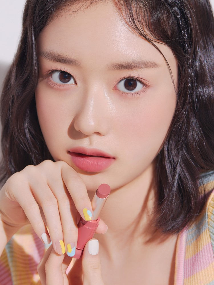 A close-up of a model holding a pink lipstick from the Etude House Fixing Tint Bar collection, showing its smooth texture on her lips against a soft background.