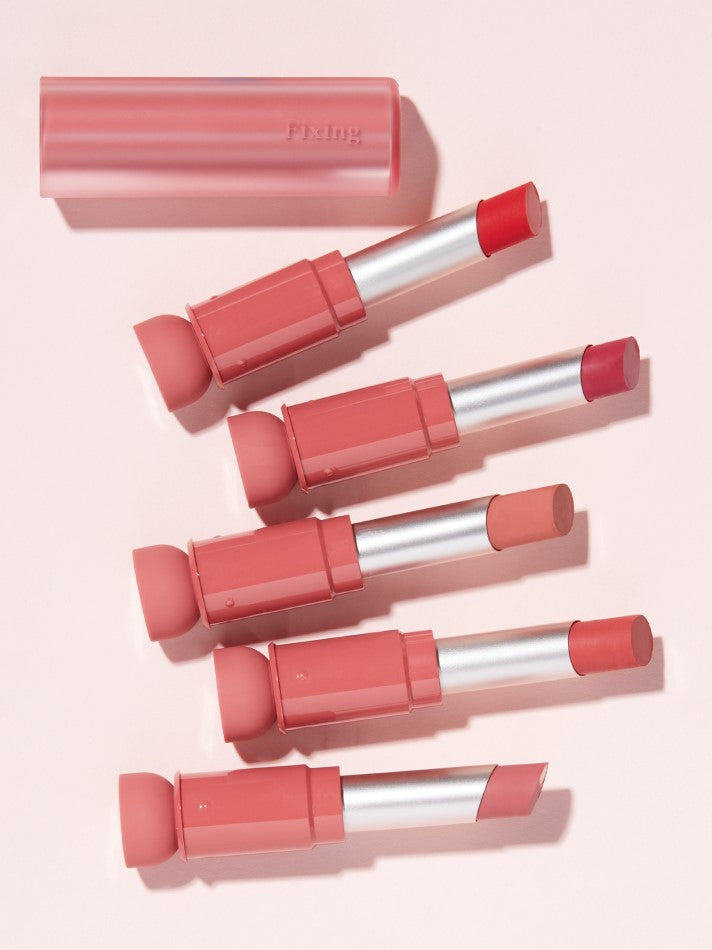 Five lipsticks from the Etude House Fixing Tint Bar collection in various pink and red shades, displayed with a clear cap labeled 'Fixing' on a soft pink background.