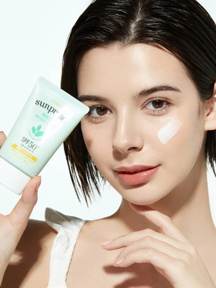 A model holds a tube of Etude House Sunprise Mild Watery Light Sunscreen, showcasing its lightweight texture on her cheek against a bright, neutral background.