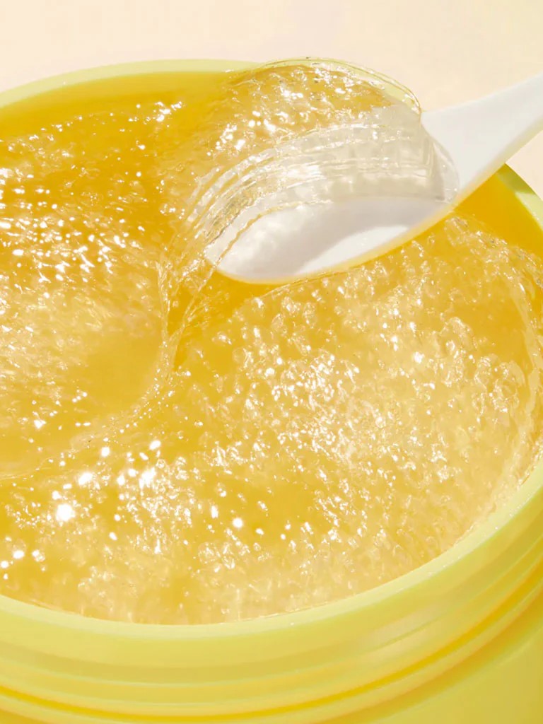 A close-up of Goodal Green Tangerine glossy yellow gel patches, with a white spatula lifting one, showcasing their texture and vibrancy.
