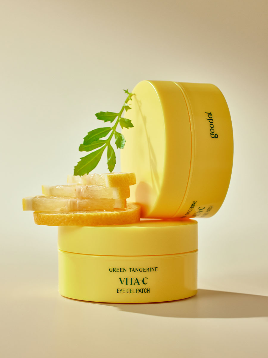 Stacked jars of Goodal Green Tangerine Vita C Eye Gel Patch, surrounded by fresh lemon slices and a green leaf, emphasizing a vibrant and refreshing skincare concept.