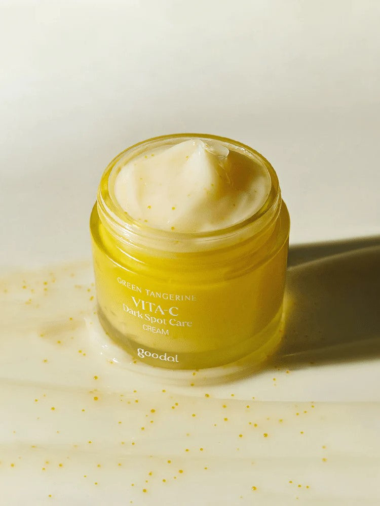A jar of Goodal Vita-C Dark Spot Care Cream in yellow, showing its creamy texture with visible tangerine pieces, set against a light background.