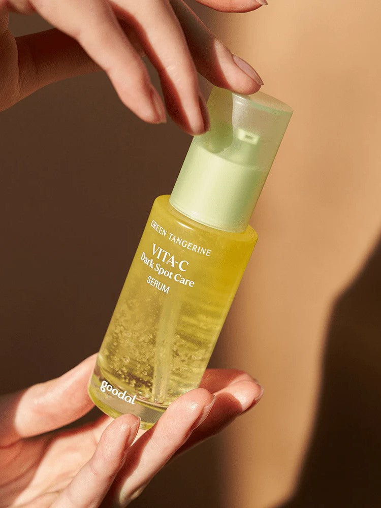 A hand holding a glass bottle of Goodal Green Tangerine Vita-C Dark Spot Care Serum, highlighting its vibrant yellow liquid.