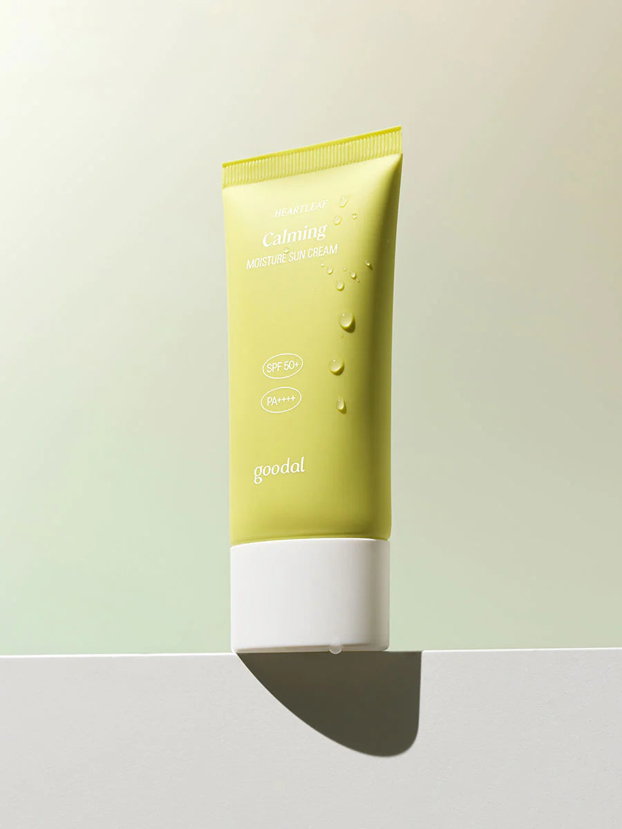 A pastel green tube of Goodal Houttuynia Cordata Calming Moisture Sun Cream with SPF 50+ and PA++++, resting on a white ledge with water droplets.