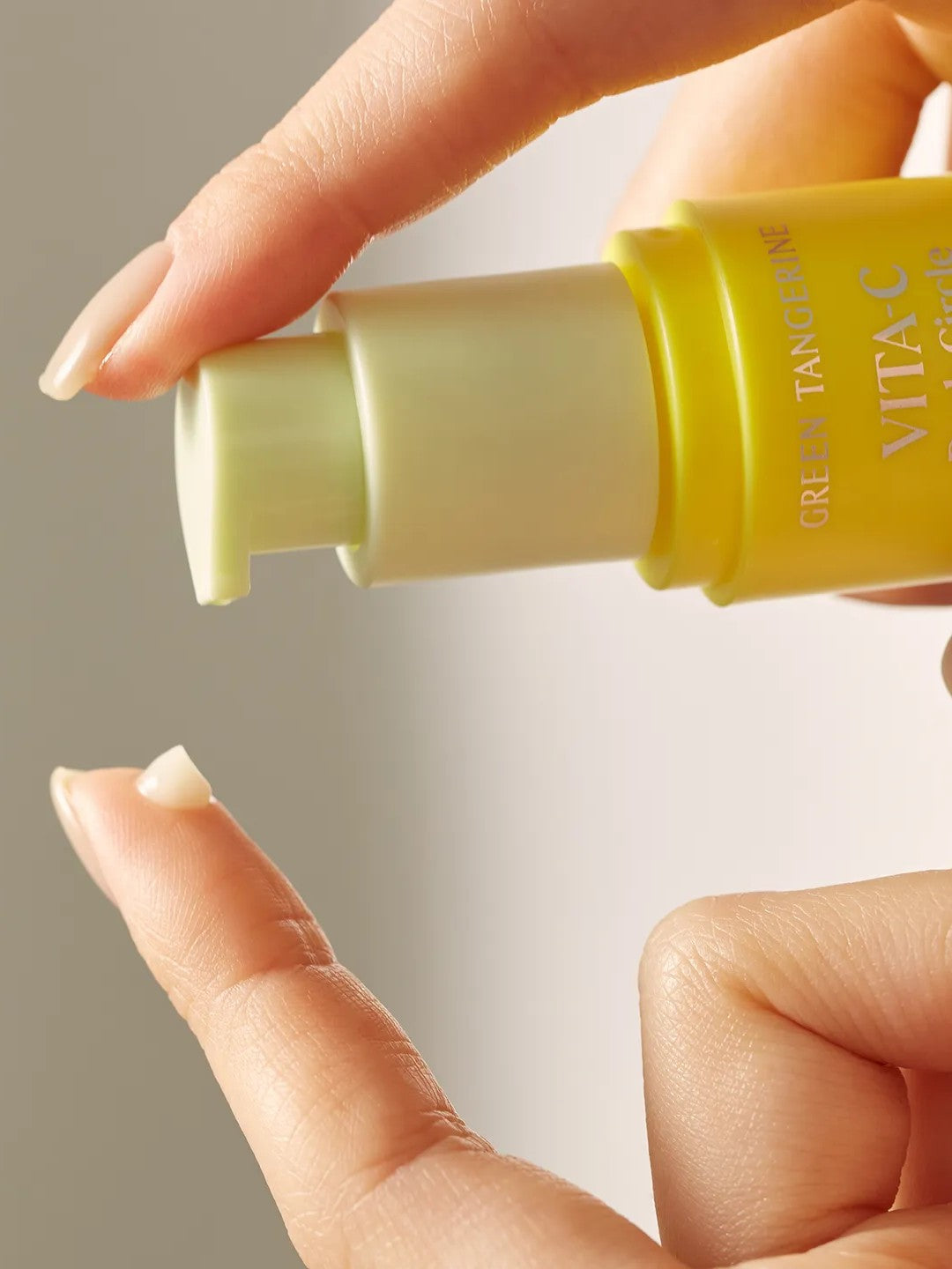 A hand holds a yellow bottle of Goodal Green Tangerine Vita C Dark Circle Eye Cream, with a droplet of cream on the fingertip, showcasing its smooth texture.