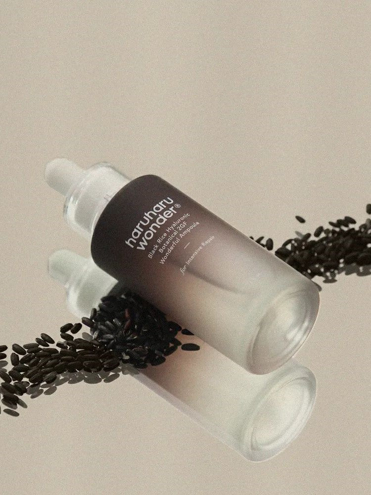 Haruharu Wonder Black Rice Hyaluronic Botanical 2GF Wonderful Ampoule surrounded by black rice grains on a soft beige background.