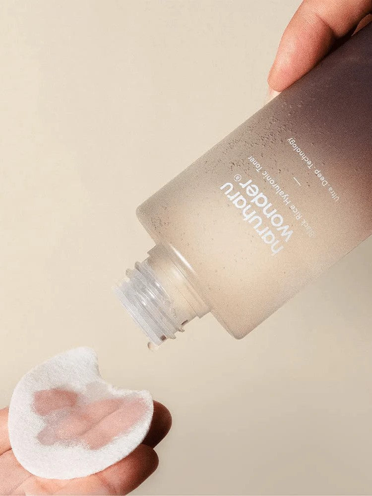 A hand holding Haruharu Wonder Black Rice Hyaluronic Toner, pouring onto a cotton pad, highlighting its lightweight texture.