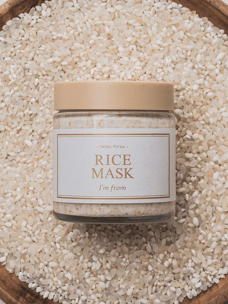 A jar of 'I'm From' Rice Mask placed on a bed of white rice in a wooden bowl, highlighting its main ingredient.